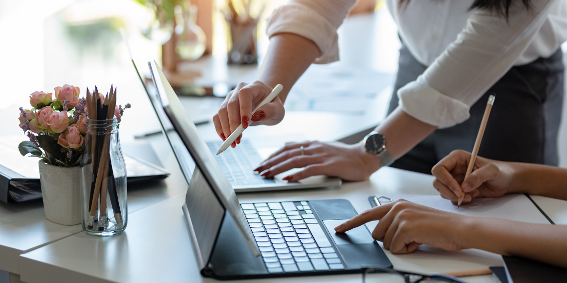 A pair of hands typing on a laptop keyboard and a second set of hands pointing to something on the screen